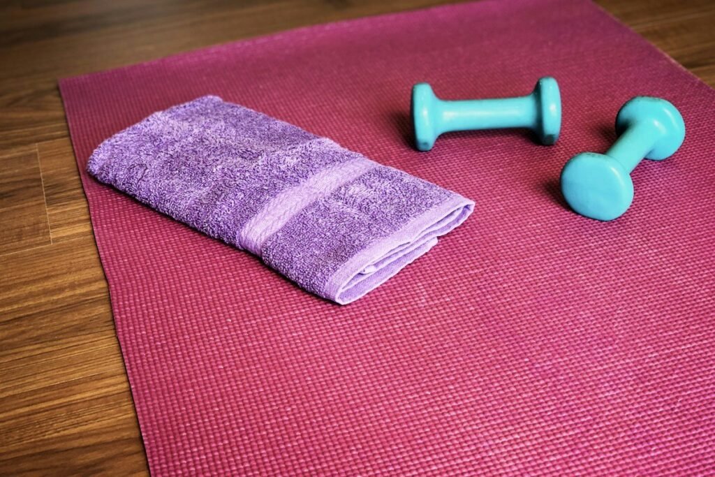 Recovery items laid out on a wooden floor, including a foam roller, a rolled towel and a handheld massage tool.